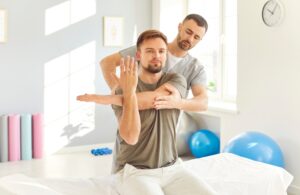 Male chiropractor or physical therapist assisting man with arm rehabilitation in clinic, representing physiotherapy and osteopathic treatment.