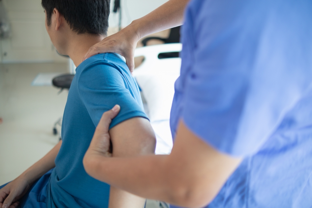 Doctor treating a man for muscle pain and inflammation in the back and shoulder, caused by overwork and physical strain, highlighting musculoskeletal care and pain management.