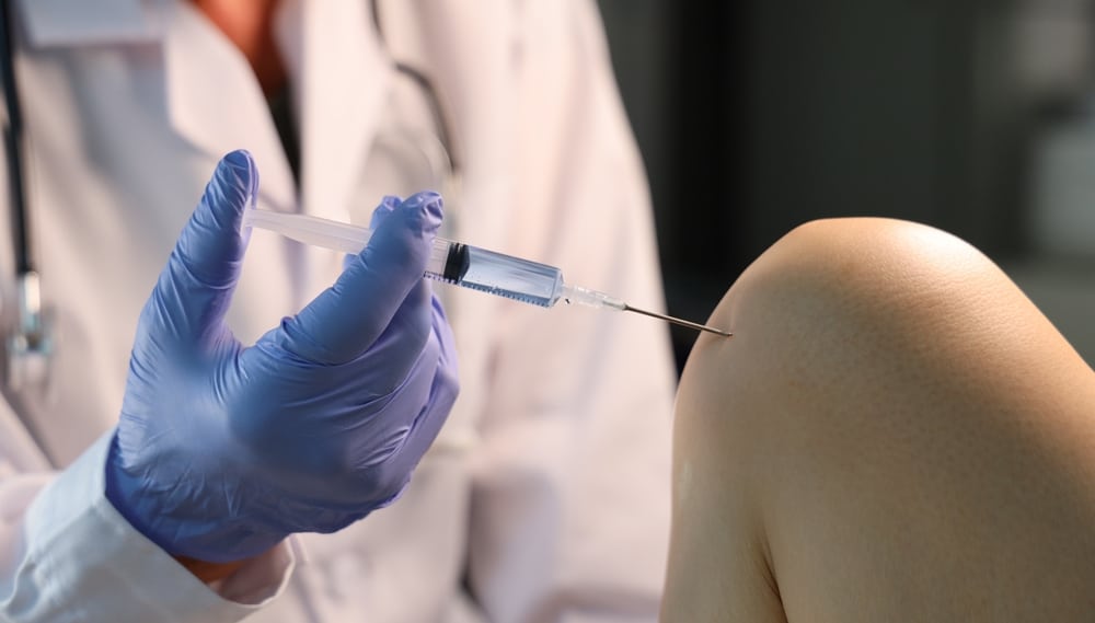 Close-up of doctor administering injection into patient’s knee for joint pain relief or orthopedic treatment.