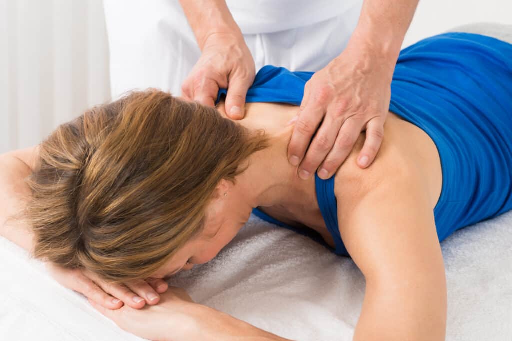 Woman in blue tank top receives back massage from a physical therapist.